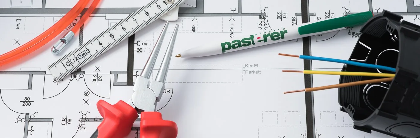 Installationsplan mit Pasterer-Kugelschreiber, roter Zange, Meterstab und einer Unterputzdose mit Leitungen