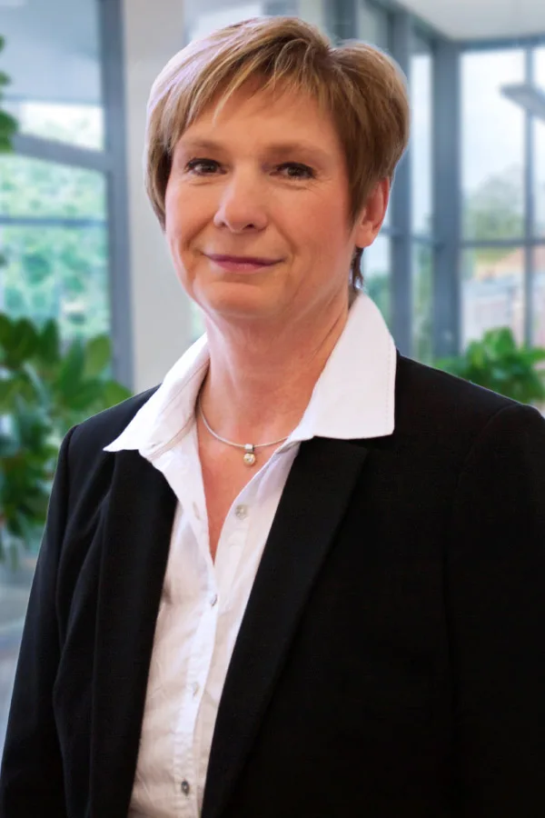 Eveline Luger-Pasterer in schwarzem Blazer und weißer Bluse vor einer Glasfront mit Pflanzen