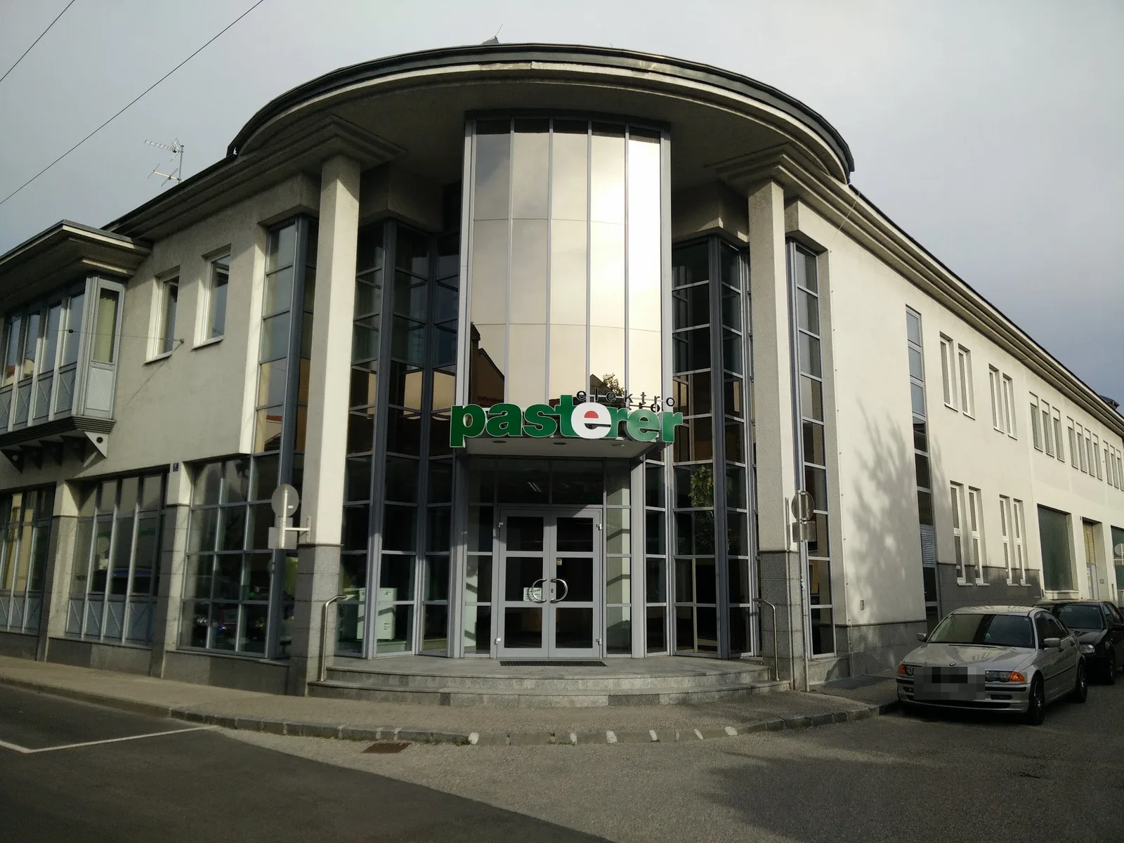 Früheres Firmengebäude mit Glasfront, runder Dachkante und der Leuchtschrift elektro pasterer über dem Eingang